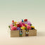 Colorful flower arrangement in a wooden box with small figurines on a light background